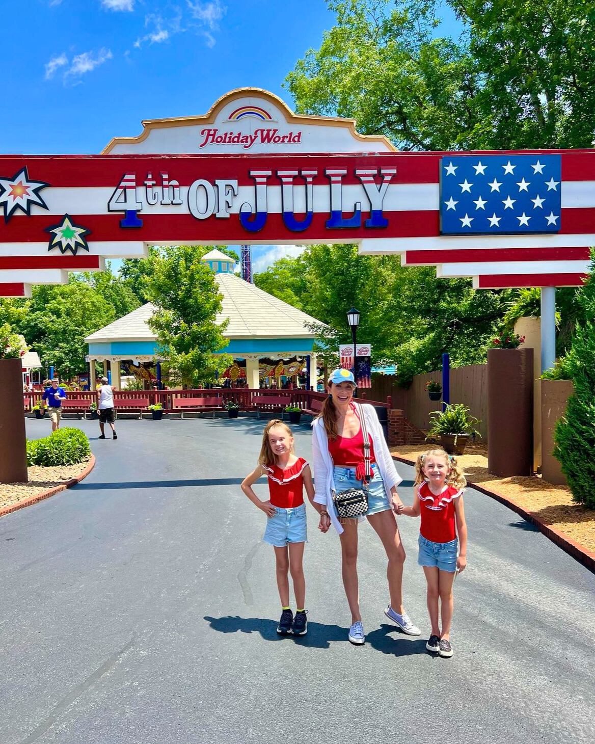 A mom and two children pose in front of the 4th of July sign in the park
