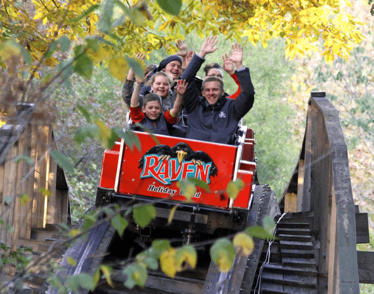 The Raven wooden roller coaster crests a hill as it careens through the woods at Holiday World.