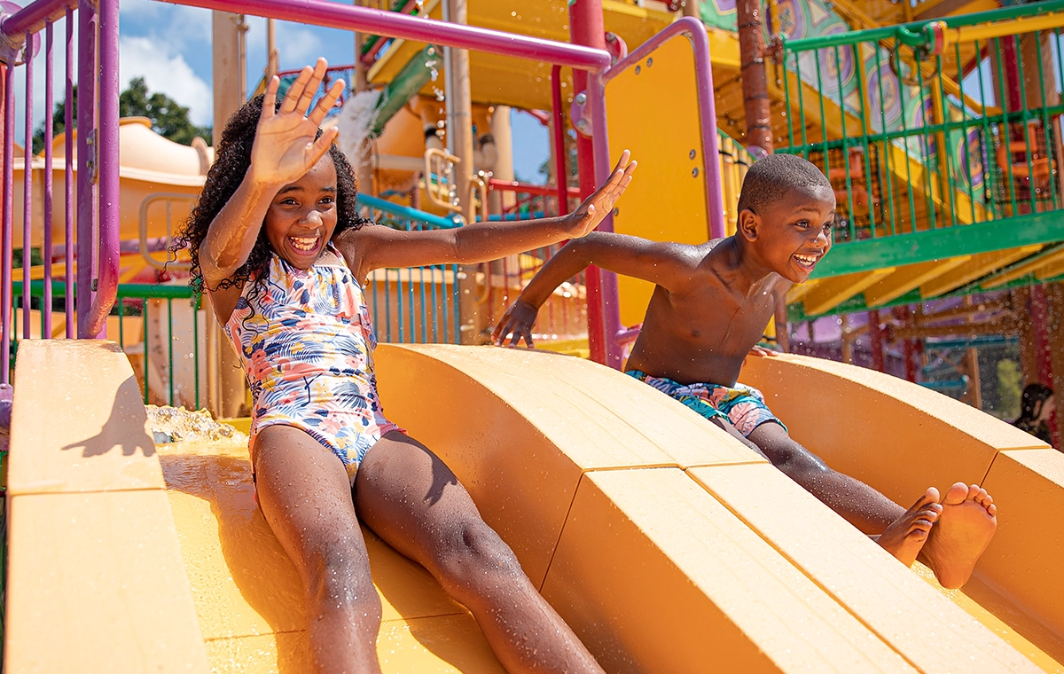 A young girl and boy sliding side-by-side at Kima Bay at Holiday World & Splashin' Safari in Santa Claus, Indiana.