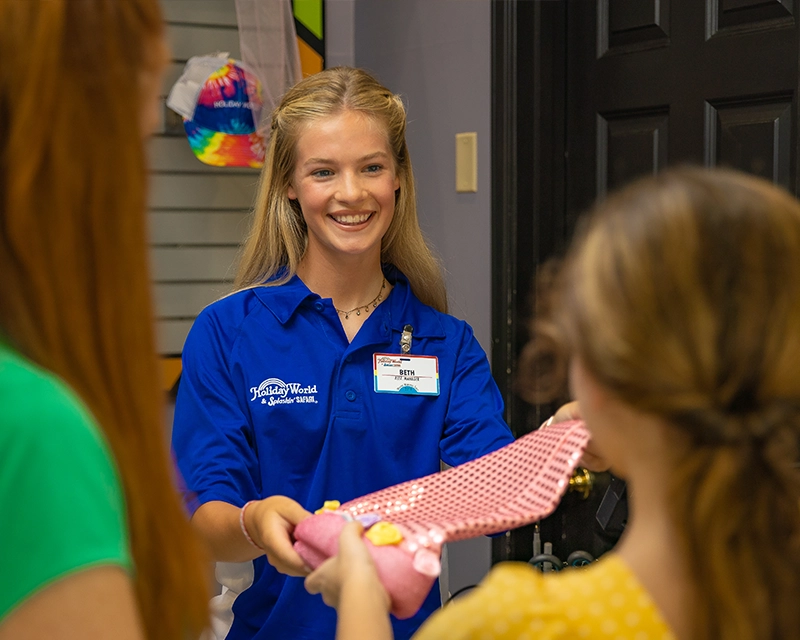 Retail Team Member helps a mother and daughter with a princess hat purchase at Spooky's Hat Shop.